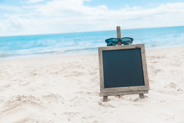  Chalk board with sunglasses on the sea beach sand summer tropical holiday concept