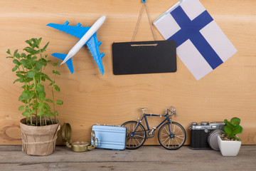 Travel time concept - blank blackboard, flag of the Finland, airplane model, little bicycle and suitcase, compass on wooden background