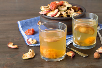 A mixture of dried fruits in a round wooden bowl and freshly prepared compote in a glass on a old table. Delicious and healthy drink.