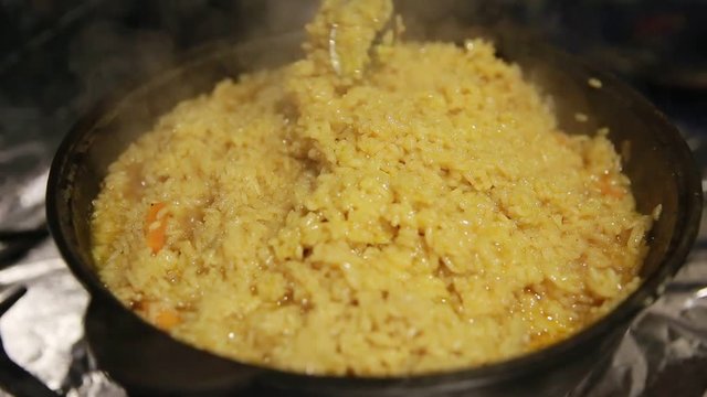 Cooking pilaf, shef gently stirs the top layer of the pilaf in cast-iron kettle