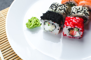 on the plate is white, lined with different rolls, sushi