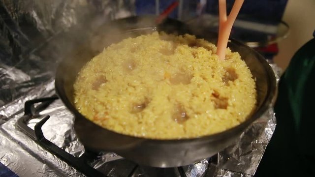 Cooking pilaf, shef makes holes for the boiling of the pilaf in cast-iron kettle