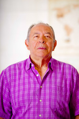 Portrait of a happy mature man wearing a purple square t-shirt in a blurred background