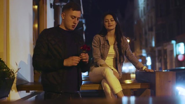 Romantic couple in love having date, he picks up the flower at the restaurant window and presents it to his beloved, she laughs charmingly. True emotions, romantic date