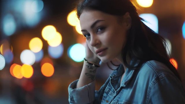 Hot young woman in jeans jacket stroking her hair, posing to camera. night city lights on the background. Enjoy the moment, positive mood, playful. Slow motion, female portrait