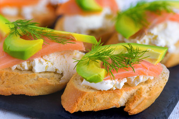 Bruschetta, snack sandwiches with white cheese, smoked salmon and pieces of avocado decorated by dill.