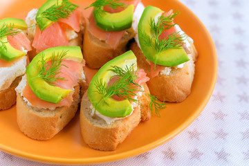Bruschetta, snack sandwiches with white cheese, smoked salmon and pieces of avocado decorated by dill.
