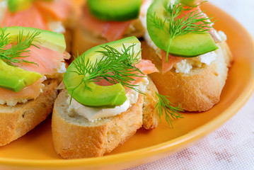 Bruschetta, snack sandwiches with white cheese, smoked salmon and pieces of avocado decorated by dill.