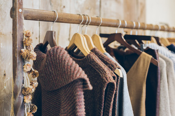 Conscious / ethical  fashion trend concept.  Warm winter ladies clothes collection with knitted jumpers, dresses and cardigans on wooden hangers. - obrazy, fototapety, plakaty