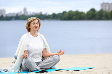 Elderly woman doing yoga on beach