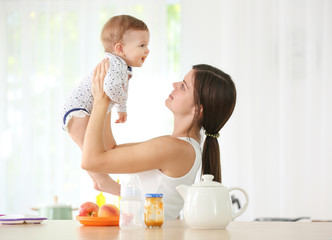 Mother holding cute baby in kitchen