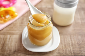Jar and spoon with healthy baby food on wooden table