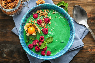 Bowl with yummy spirulina smoothie and bottle of drink on wooden table. Healthy vegan food concept