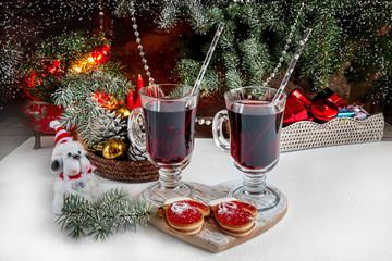 Two glasses of mulled wine at the Christmas table in the background garlands and fir branches. The dog - Symbol of the year. Snow.