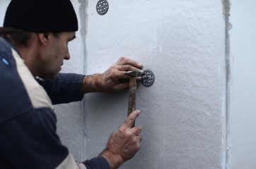 An elderly workman clogs a dowel into a plastic umbrella mount in a styrofoam wall. The process of fixing expanded polystyrene plates. Warming of the facade of the building