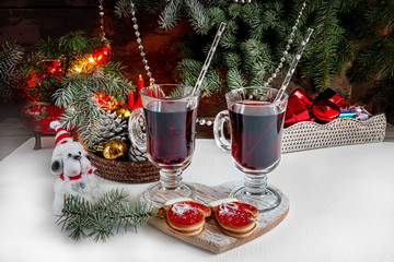 Two glasses of mulled wine at the Christmas table in the background garlands and fir branches. The dog - Symbol of the year. Snow. The horizontal frame.