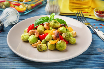 Plate with baked Brussels sprouts, pepper and nuts on table