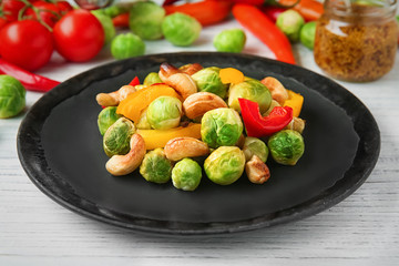 Plate with baked Brussels sprouts, pepper and nuts on table