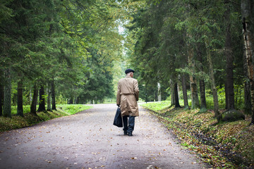 Old man in brown coat walks in park in autumn.
