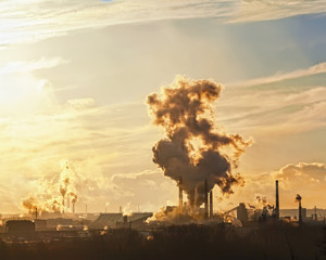the pipes of a large plant smoke in the sky