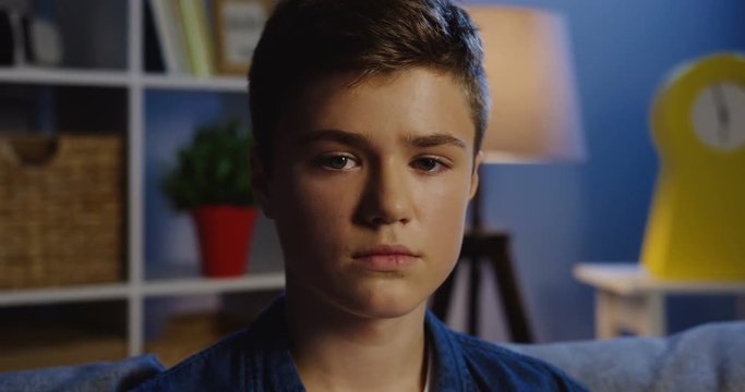 Portrait of the cute teen boy turning his head into the camera and smiling in the comfortable cozy room in the evening. Close up. Outdoor