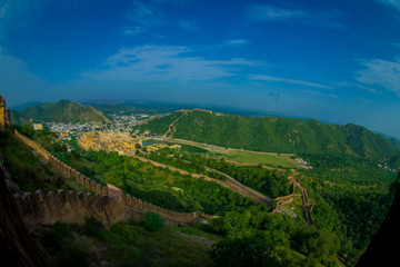 Fototapeta na wymiar Beautiful landscape of Amber Fort with green trees, mountains and small houses near Jaipur in Rajasthan, India. Amber Fort is the main tourist attraction in the Jaipur area