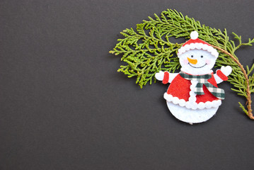 Christmas frame from pine branch and snowman figure on black background. Top view. Space for text.