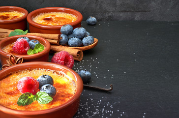 Creme brulee with berries and ingredients on dark stone, space