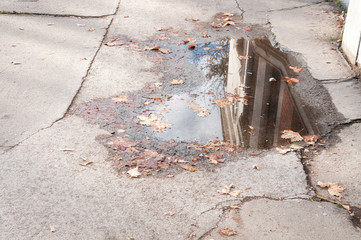 Pond of rain water in the hole on the damaged sidewalk