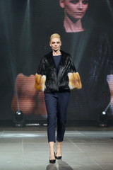 Beautiful fashion model  walks on runway in fur coat with online screen on background