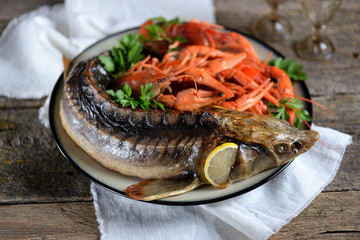 Baked whole sturgeon with boiled crawfish and lemon on an old wooden background. Rustic style.