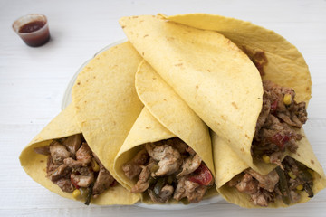 Fajitas consisting of chicken stew with red and green pepper, with red onion, pickled cucumber and spices wrapped in a corn cake.