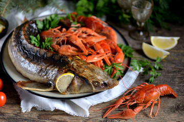 Baked whole sturgeon with boiled crawfish and lemon on an old wooden background. Rustic style.