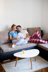 Lovely happy young couple lying on the sofa and laughing while drinking juice in pajamas in the morning.