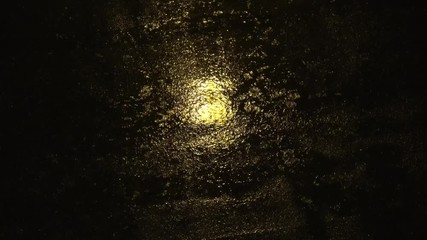Top-down view of rainy street at night showing the dark paved road and the reflection of the city lighting and rain droplets falling down typical urban scene during sad rainy evenings 4k quality