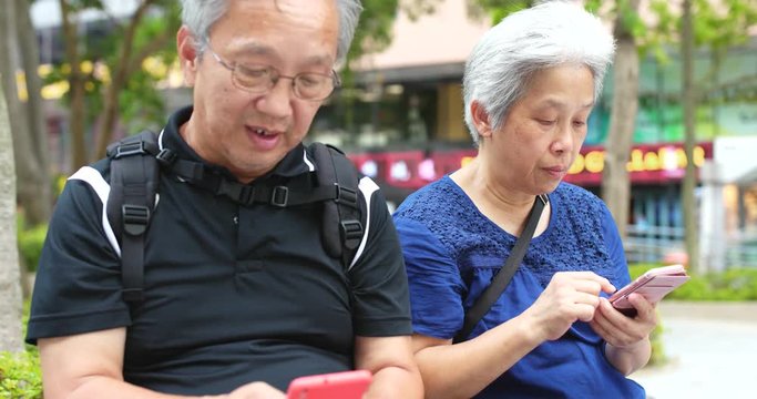 Asian senior couple use of cellphone in park