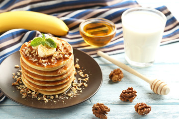 Tasty pancakes with walnuts, bananas and glass of milk on wooden plate