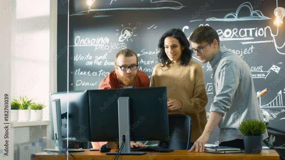 Poster Team of Creative Designers Look at Computer Monitors and Discuss Their Project. They Work in the Stylish Office with Chalkboard Wall. Shot on RED EPIC-W 8K Helium Cinema Camera.