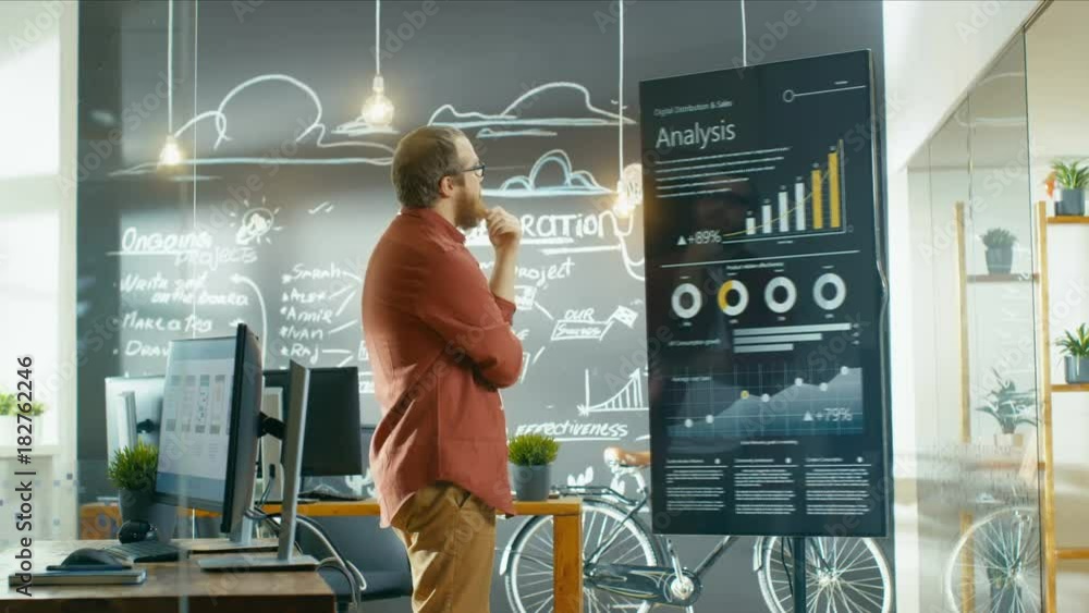 Poster Marketer Looks at Interactive Touchscreen Whiteboard Showing Latest Graphs and Charts on Statistical Growth. He Works in the Creative Office. Shot on RED EPIC-W 8K Helium Cinema Camera.