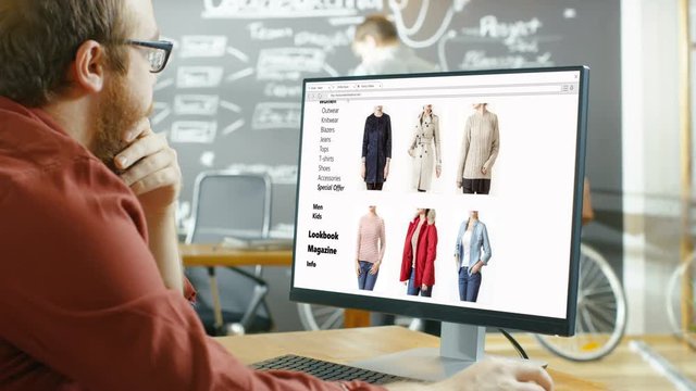 Web Designer Works on a Website for Online Retail Clothing Store. He and Colleagues Work in Stylish Creative Agency Studio with Blackboard. Shot on RED EPIC-W 8K Helium Cinema Camera.