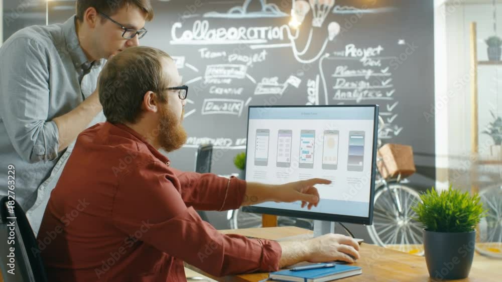 Poster Two Male Mobile Game Application Developers Talk while Working on a Personal Computer, Designing Wireframe. Coworkers Work in the Creative Indie Studio. Shot on RED EPIC-W 8K Helium Cinema Camera.