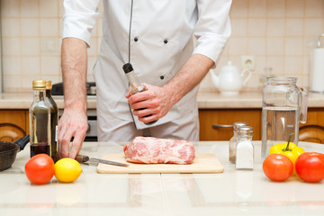 Man's hand holds bottle with souce. Professional cook prepare the meat