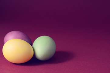 Trendy photo of Three multi colored easter eggs on a dark purple background.