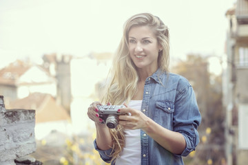 Outdoor smiling lifestyle portrait of pretty young woman with retro camera on terasse