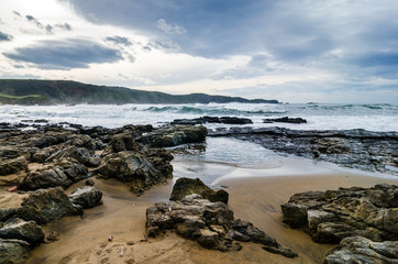 Fototapeta na wymiar Waves on the coast in Verdicio beach in Asturias, Spain.Choppy sea in a virgin beach with rocks and foam at evening