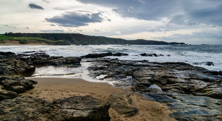 Fototapeta na wymiar Waves on the coast in Verdicio beach in Asturias, Spain.Choppy sea in a virgin beach with rocks and foam at evening