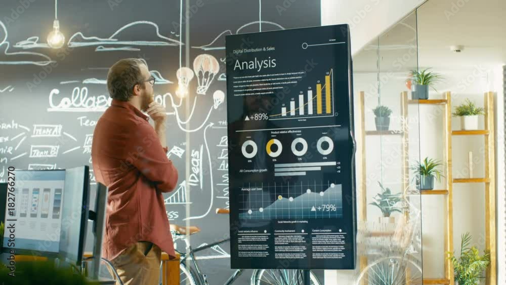 Poster Marketer Looks at Interactive Touchscreen Whiteboard Showing Latest Graphs and Charts on Statistical Growth. He Smooths His Beard in Thinking Gesture. Shot on RED EPIC-W 8K Helium Cinema Camera.