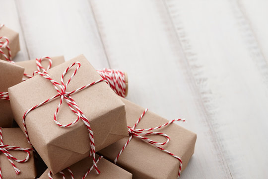Christmas gift or present boxes wrapped in kraft paper with striped baker's twine string on white wooden background, copy space
