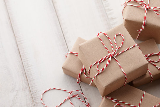 Christmas gift or present boxes wrapped in kraft paper with striped baker's twine string on white wooden background, copy space