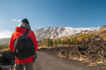 Hiker on a lavic path in the northern side of Mount Etna, Italy, and the snowy volcano